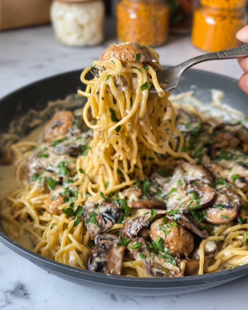 A close-up of creamy pasta with several mixed layers: the bottom layer is a smooth white creamy sauce, the middle layer has light yellow spaghetti noodles twisted and coated with sauce, and the top layer includes browned mushroom pieces with a slightly soft texture and chopped green herbs sprinkled all over, sitting inside a dark pan on a white marbled surface. A woman's hand holding a fork lifts a portion of the yellow noodles wrapped around it with mushrooms and herbs attached, and the background shows blurred jars of orange lentils, white rice, and macaroni. photo taken with an iphone --ar 4:5 --v 7