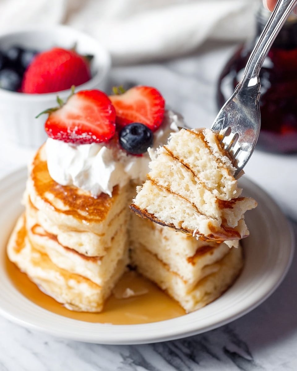 A stack of three thick, golden brown pancakes sits on a white plate, with syrup pooling around the bottom. On top of the stack is a dollop of white whipped cream, topped with two red strawberry slices and one dark blue blueberry. A woman's hand holds a fork at the front, lifting a bite-sized piece of the fluffy pancakes that show a soft, light inside. In the background on a white marbled surface, there is a small white bowl with more blueberries and a strawberry slice, and a dark bottle with syrup. photo taken with an iphone --ar 4:5 --v 7