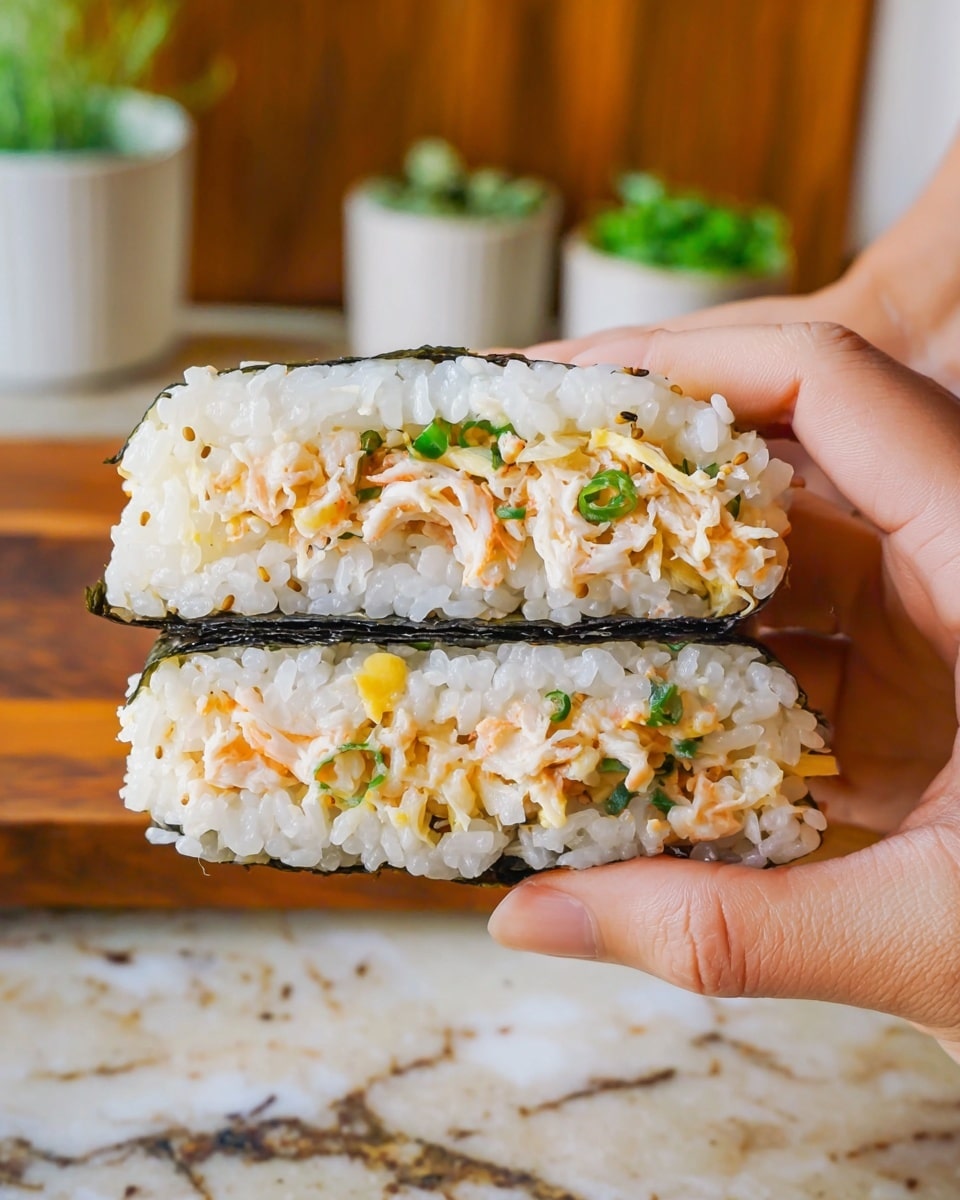 A close-up of a Japanese rice sandwich held by two woman's hands. The sandwich has three visible layers: the outer layers are white rice mixed with small green herbs and yellow bits, and a thin black seaweed sheet wrapped around the middle of the rice. The center layer contains pale orange and white shredded crab sticks mixed with green onions. The background features a blurred wooden surface and white marbled texture with some green herbs in white containers. Photo taken with an iphone --ar 4:5 --v 7