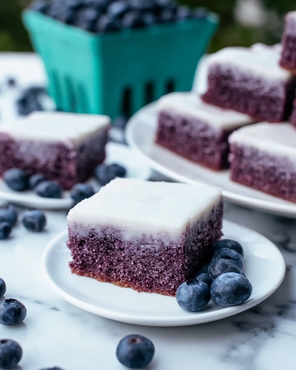 Two square pieces of purple blueberry cake stacked on top of each other with a thin white frosting layer on the top of both pieces. The cake texture looks soft and moist. Around the slices, fresh dark blue blueberries are scattered on a white marbled surface. Behind the cake, there is a turquoise carton filled with blueberries, slightly out of focus. The background is light and blurred with hints of more blueberry cake in the distance. Photo taken with an iphone --ar 4:5 --v 7