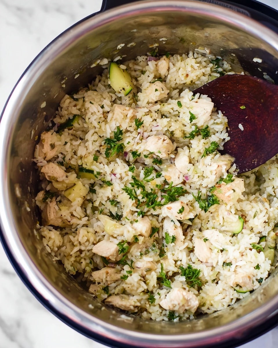 The image shows a close-up view of a metal pot filled with cooked rice mixed with small white pieces of chicken, light green slices of zucchini, and small bits of red onion. There are sprinkles of fresh green herbs like parsley scattered on top, adding a touch of color. A dark wooden spoon is partly buried in the pot, indicating the dish has been stirred. The pot is placed on a white marbled surface. photo taken with an iphone --ar 4:5 --v 7