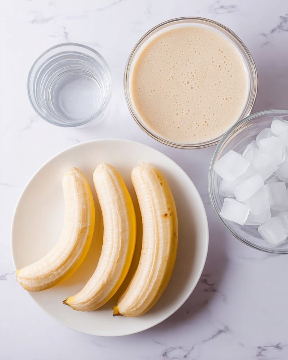The image shows three peeled bananas placed side by side on a white plate at the bottom center of the frame. Above the plate, there is a clear bowl filled with light beige batter or cream, with a smooth and slightly bubbly texture. To its right, there is a small glass of clear liquid, likely water. At the far right, there is a transparent bowl filled with several irregular ice cubes. The background is a white marbled surface. photo taken with an iphone --ar 4:5 --v 7