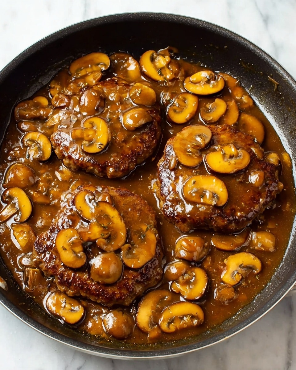 The image shows a close-up of a white bowl filled with soft, creamy mashed potatoes as the bottom layer. On top of the mashed potatoes, there is a thick, brown hamburger patty covered in a shiny mushroom sauce with many sliced mushrooms spread evenly over the patty and around the edges of the potatoes. The sauce has a smooth, glossy texture that reflects light. In the background, a pan with more mushroom sauce and mushrooms is slightly blurred, all set on a white marbled surface. Photo taken with an iphone --ar 4:5 --v 7
