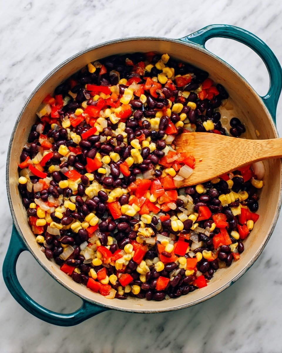 A large round pot with deep teal handles contains a colorful mix of cooked black beans, bright yellow corn kernels, small diced red bell peppers, and soft translucent onion pieces, all evenly spread and stirred by a wooden spatula on the right side of the pot, against a white marbled surface background photo taken with an iphone --ar 4:5 --v 7