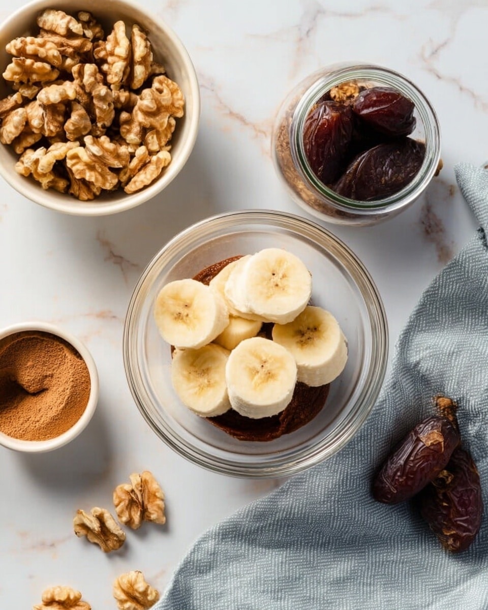 The image shows a clear glass bowl on a white marbled surface, filled with sliced banana pieces on top and a dark brown paste beneath them, likely dates or chocolate spread. Around the bowl are three containers: a white bowl filled with whole walnuts to the upper left, a white bowl with brown powder, possibly cinnamon, to the lower left, and a small glass jar filled with whole dark brown dates to the right. A soft gray cloth is draped partially under the jar and extends onto the surface. Photo taken with an iphone --ar 4:5 --v 7