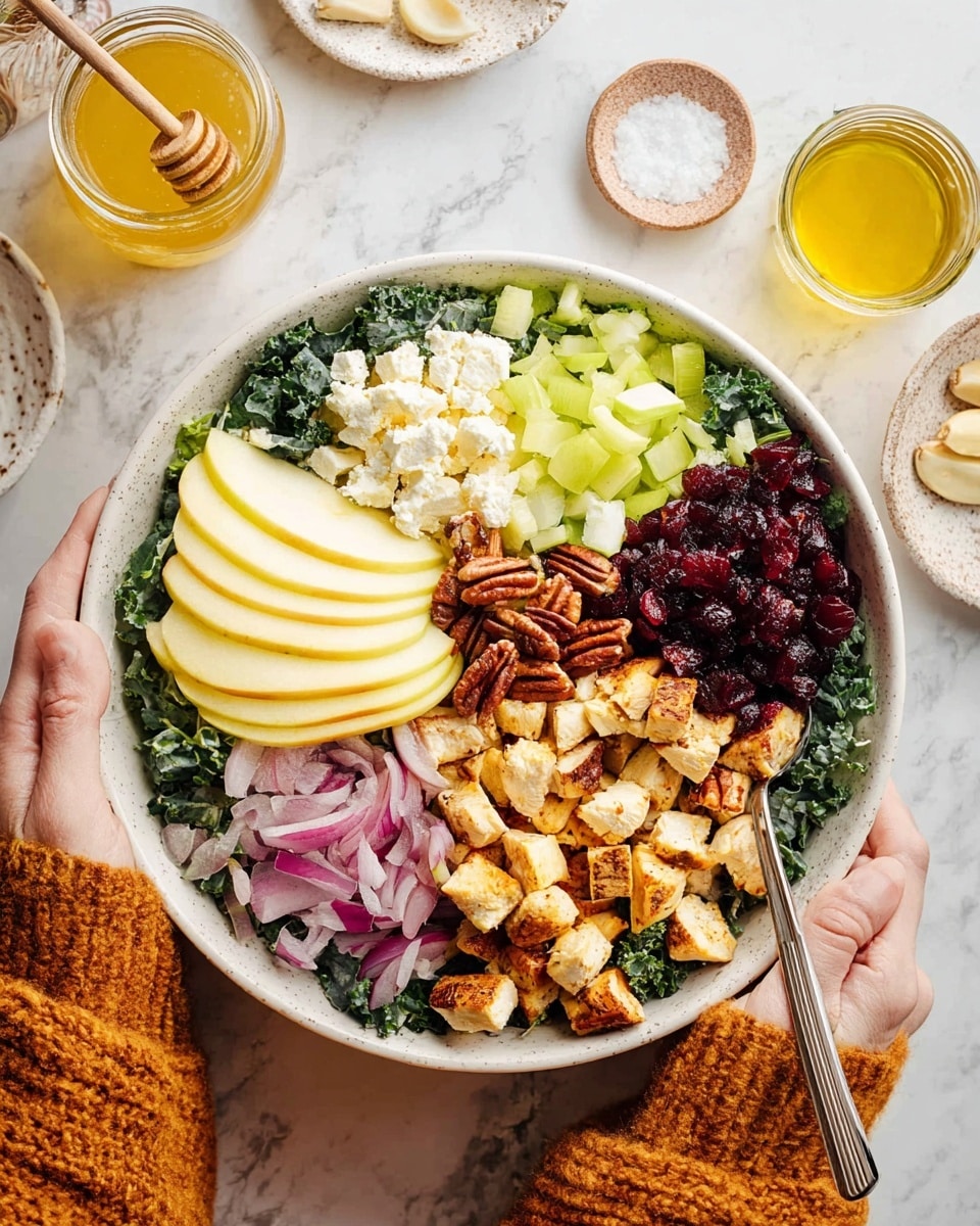 A white bowl filled with a colorful salad arranged in sections on a white marbled surface. The base layer is dark green kale leaves filling most of the bowl. On top, there are seven groups: white crumbly cheese on the left, light green diced celery at the top right, medium brown pecan halves near the top center, thin slices of pale green-yellow apple on the left and right sides, thin purple onion slices next to the right apple, juicy dark red dried cranberries near the bottom center, and in the middle are golden brown grilled chicken cubes. A woman's hands in a warm orange knitted sweater hold two spoons inside the bowl from left and right sides. Around the bowl are a glass jar with honey or dressing, a glass of light yellow olive oil, a small plate of garlic cloves, and a small white plate with salt. Photo taken with an iphone --ar 4:5 --v 7