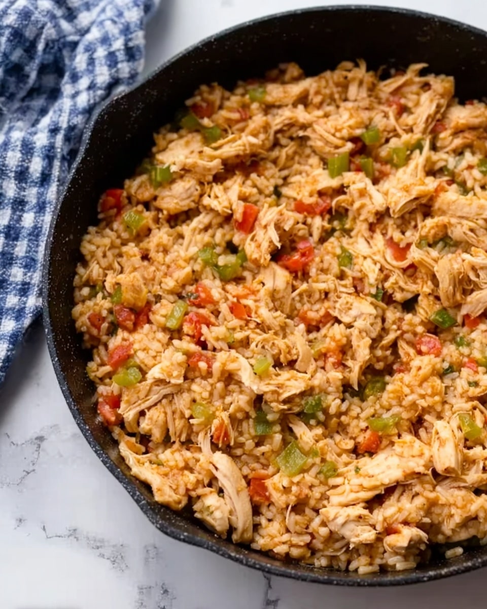 A black pan filled with a mixed dish made of shredded cooked chicken, brown rice, small pieces of red bell pepper, and bits of green bell pepper. The rice looks moist and well mixed with the chicken and vegetables. The pan sits on a white marbled surface, and there is a blue and white checkered cloth partly visible in the top left corner. The colors in the dish include light brown from the rice and chicken, red from the bell pepper, and green from the other pepper pieces, creating a warm and inviting look. photo taken with an iphone --ar 4:5 --v 7