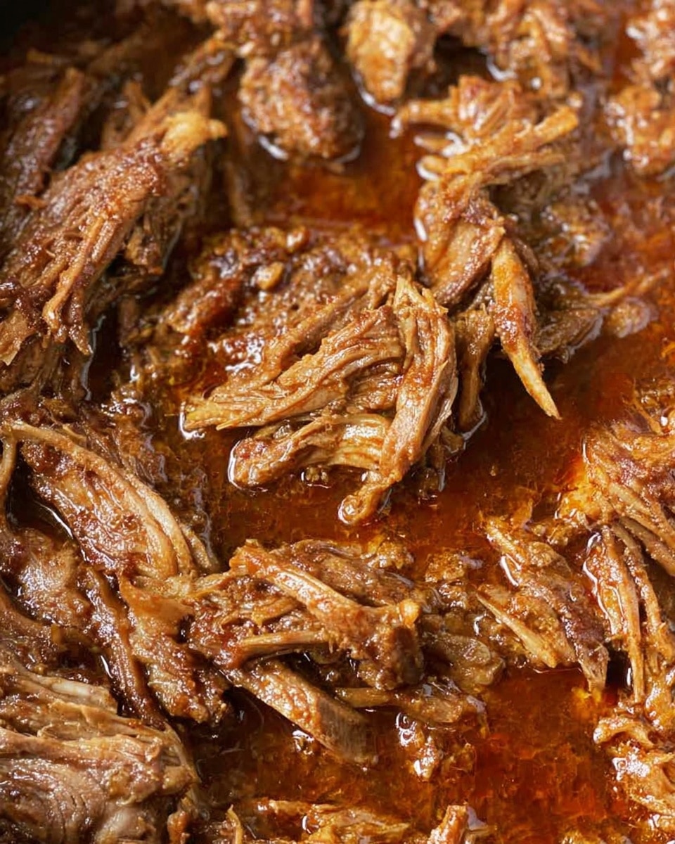 The image shows a close-up of shredded cooked meat soaked in a rich, dark brown sauce with a slightly reddish oil sheen. The meat appears tender with visible stringy textures and soft layers, all mixed evenly with the sauce. The background features a white marbled surface. Photo taken with an iphone --ar 4:5 --v 7