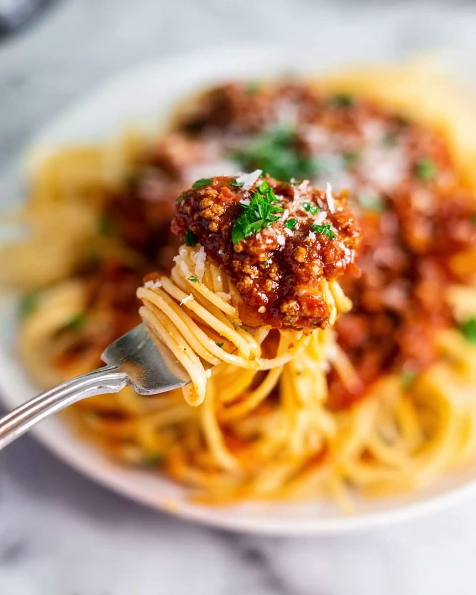 A close-up photo of a fork holding a bite of spaghetti with thick meat sauce on top. The spaghetti looks cooked and light yellow in color, twisted around the fork. The meat sauce is dark red with small chunks of ground meat and bits of tomato, sprinkled with small green parsley leaves and grated white cheese. Below the fork, there is a white plate filled with more spaghetti and sauce in the background, placed on a white marbled surface. Photo taken with an iphone --ar 4:5 --v 7