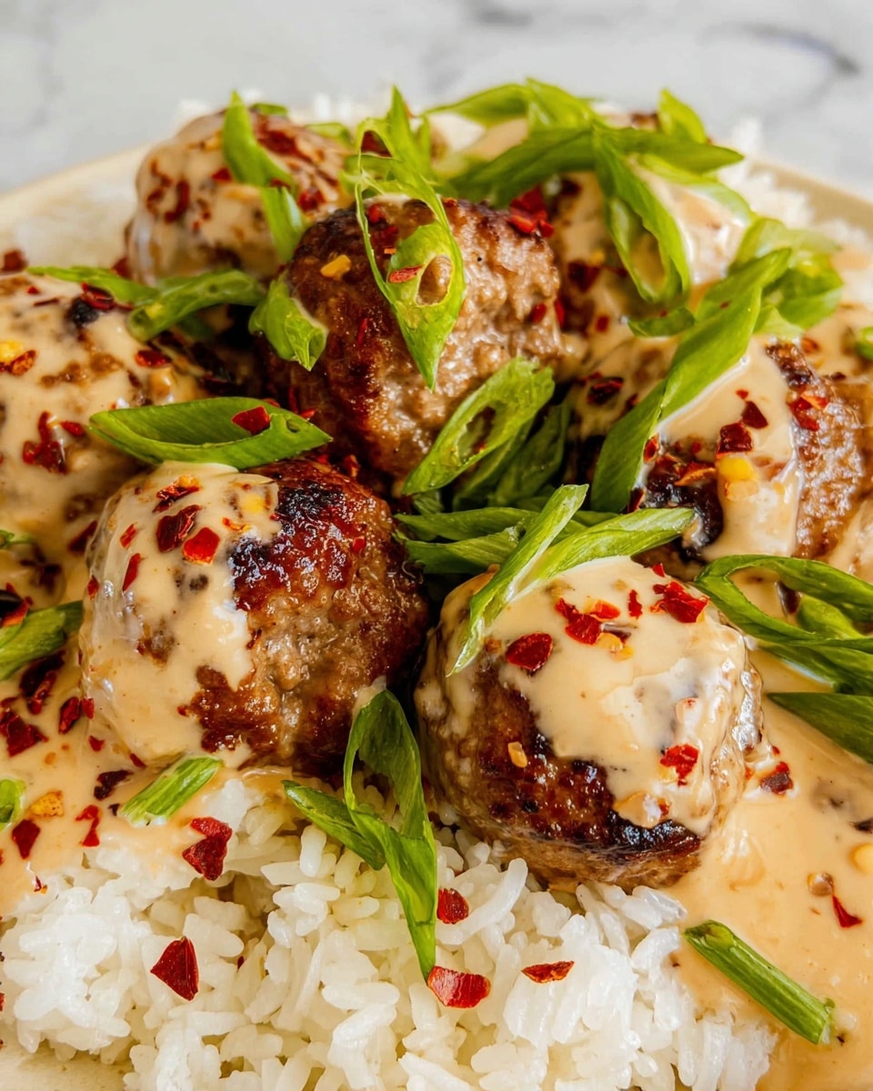 The image shows a close-up of a white plate filled with white rice at the bottom, with several brown meatballs placed on top. The meatballs are covered with a creamy light brown sauce that has dark red chili flakes sprinkled over it. Bright green sliced scallions are scattered both on the meatballs and rice, adding a fresh touch. The plate sits on a white marbled surface. photo taken with an iphone --ar 4:5 --v 7
