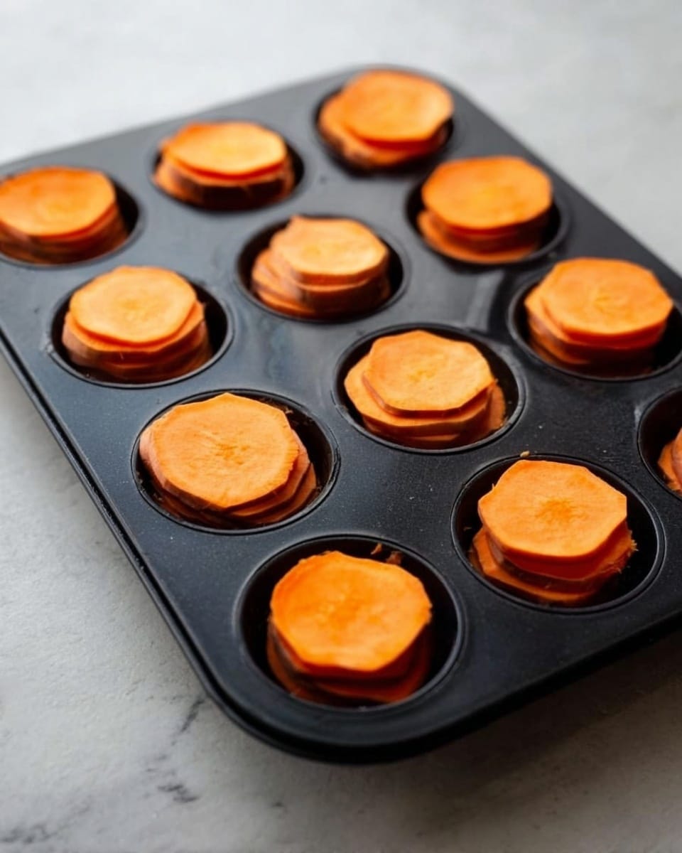 The image shows a black muffin tray with twelve cups, each filled with several thin, round slices of orange sweet potato stacked in small layers. Each sweet potato stack is about the same height, and the slices are smooth with a bright orange color. The tray sits on a white marbled surface, giving a clean and simple background. photo taken with an iphone --ar 4:5 --v 7