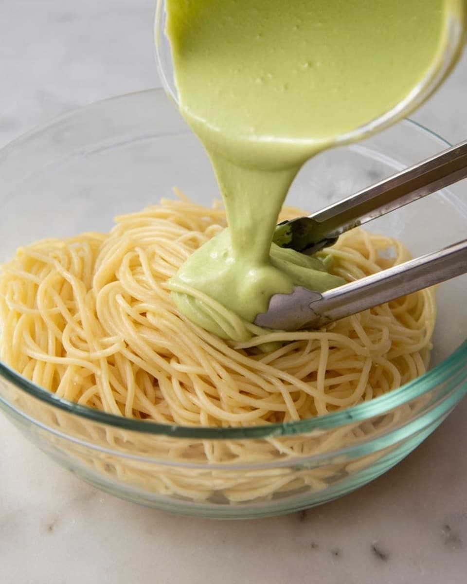 A close-up view inside a clear blender container filled with many fresh cilantro leaves, bright green with their stems, arranged loosely and filling about half of the container. From the top left, a white creamy liquid is pouring down into the blender, covering some cilantro leaves and creating a smooth contrast to the green texture. The inside walls of the blender show light yellow splashes from previous blending. The whole scene is set on a white marbled surface. Photo taken with an iphone --ar 4:5 --v 7