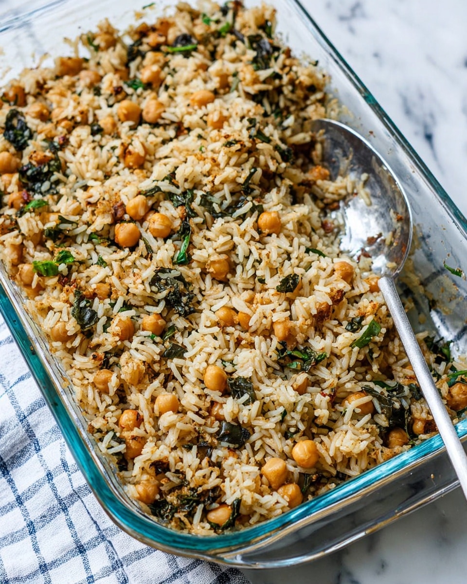 The image shows a black pan filled with a mix of cooked light beige chickpeas and bright green chopped spinach. The spinach leaves are soft and slightly wilted, covering much of the chickpeas beneath. Small pieces of translucent cooked onion are scattered through the dish, adding texture. A silver spoon peeks out from the bottom left in the pan. The pan sits on a white marbled surface with a beige cloth and a blue-and-white checkered cloth partially visible above it. To the right, there is the edge of a white dish or cup. Photo taken with an iphone --ar 4:5 --v 7