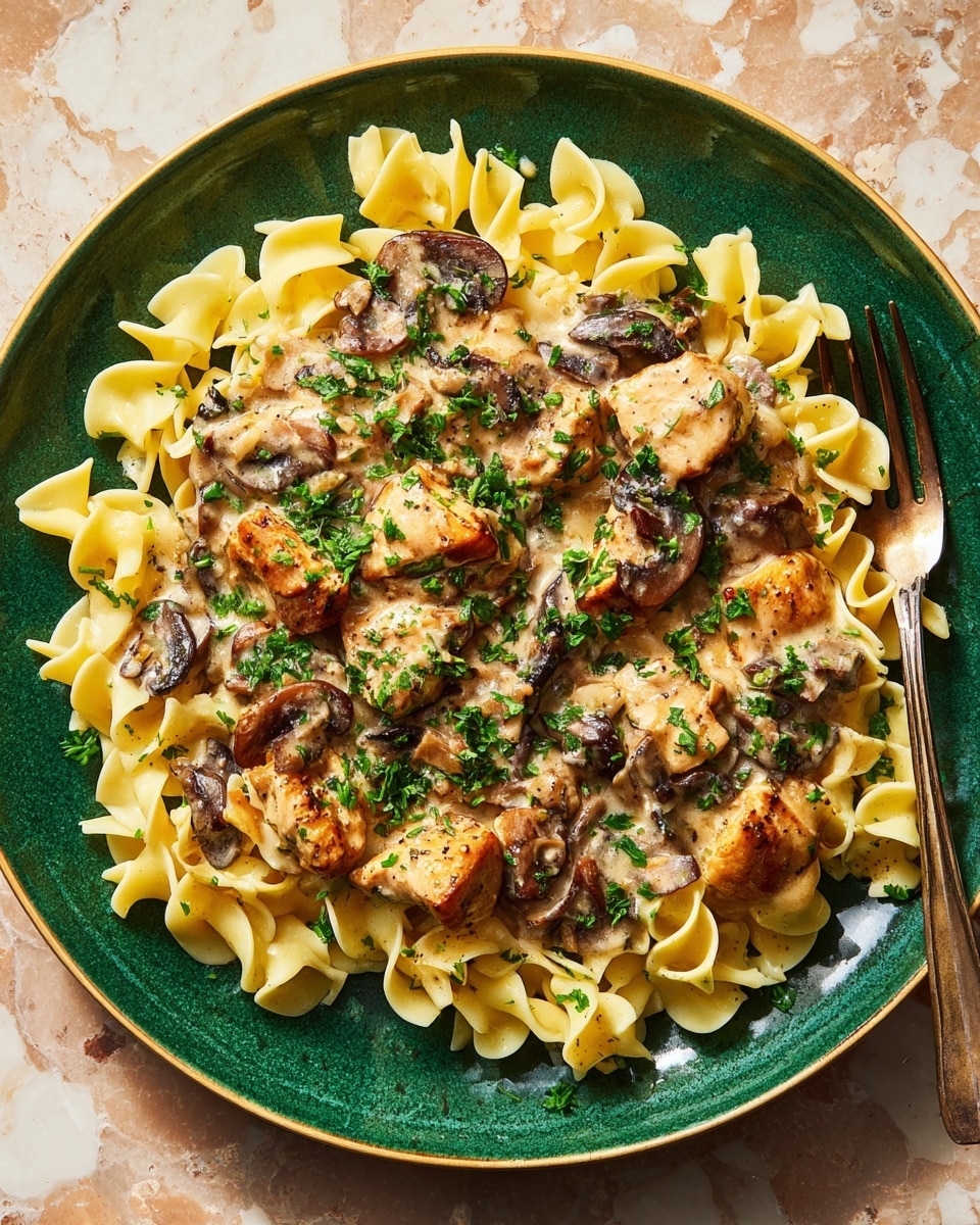 A white marbled surface holds a green plate filled with three layers: the bottom layer is pale yellow egg noodles with a ruffled texture arranged evenly across the plate; on top, there are browned chicken pieces with a slightly crispy texture scattered around; the top layer is a creamy beige sauce with small dark mushroom slices and finely chopped green parsley sprinkled all over, adding brightness. photo taken with an iphone --ar 4:5 --v 7