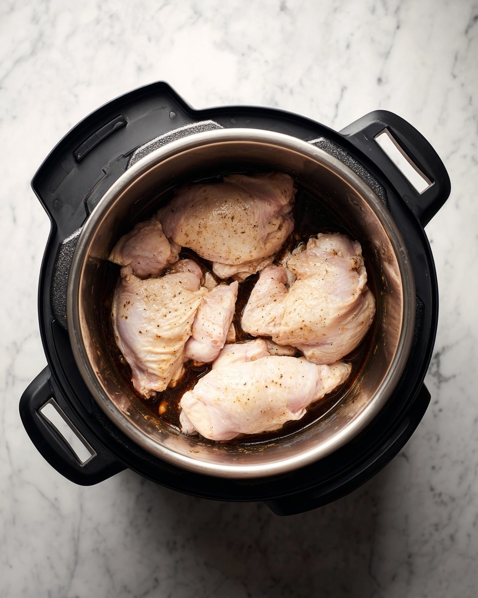 Inside a round electric cooker with black handles, four pieces of raw chicken with pale pink skin lie spread out on a dark brown sauce coating the base. The cooker’s inner pot is light-colored with some sauce stains along the sides. The background surface is a white marbled texture. Photo taken with an iphone --ar 4:5 --v 7