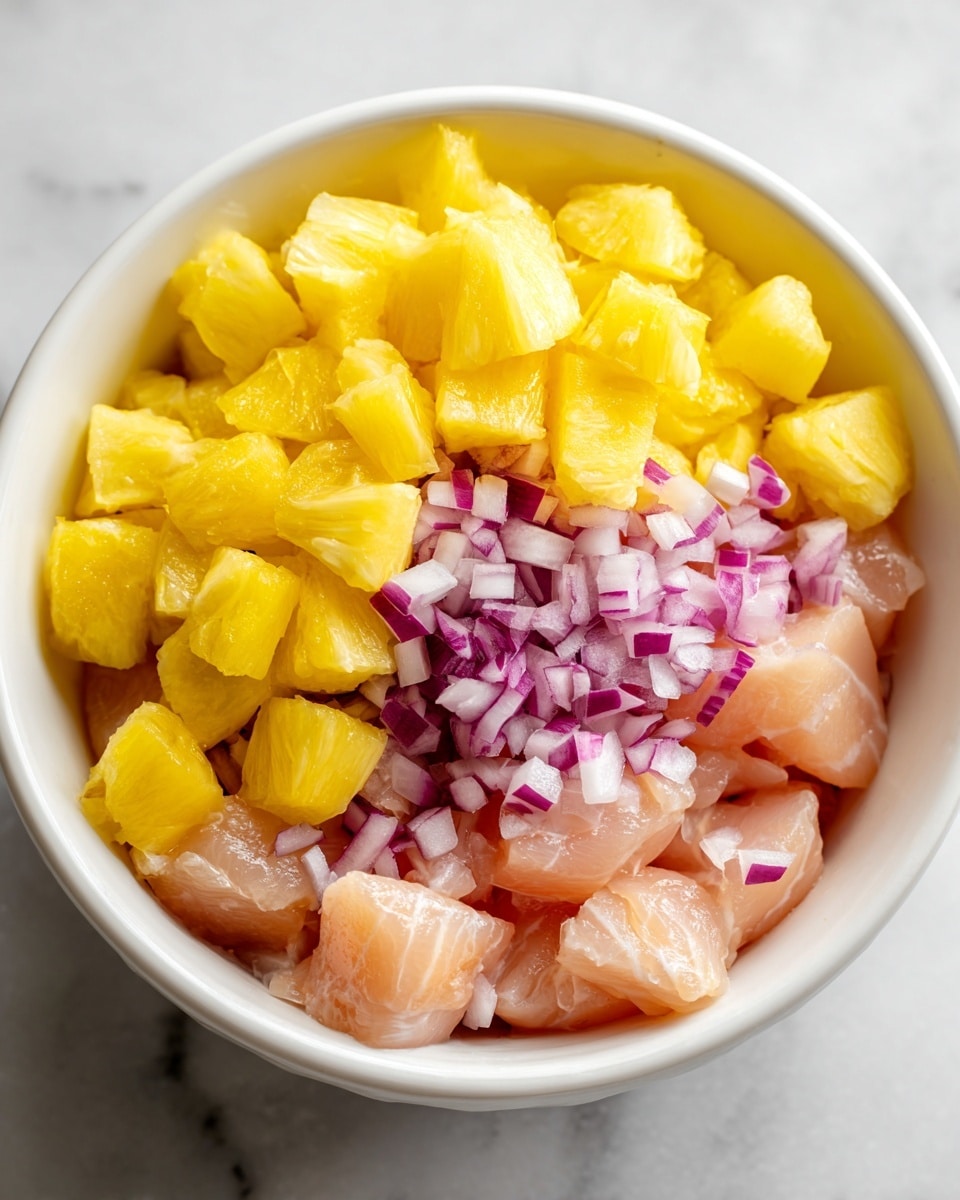 The image shows a close-up of a white bowl filled with three main layers. The bottom layer is chopped raw chicken pieces with a pale pink color and smooth texture. On top of the chicken, there is a thin layer of small diced red onion pieces, red with a slightly glossy surface. The top layer is made up of many small, bright yellow pineapple chunks covering the whole bowl. The bowl sits on a white marbled surface. photo taken with an iphone --ar 4:5 --v 7