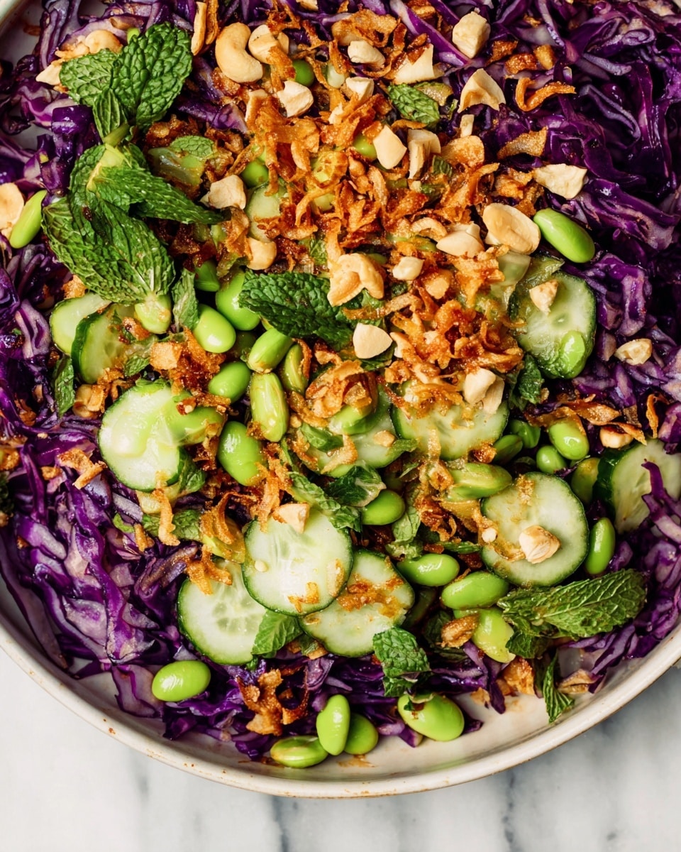 A colorful salad composed of three main layers: the bottom layer of thinly sliced purple cabbage giving a rich violet color with crisp texture; the middle layer of bright green edamame beans and sliced cucumbers, round and fresh with a light green hue; and the top layer sprinkled with golden fried shallots and chopped cashew nuts, adding crunchy texture and warm brown tones. Fresh mint leaves add small pops of deep green. The salad sits against a white marbled background, highlighting the vibrant colors. photo taken with an iphone --ar 4:5 --v 7