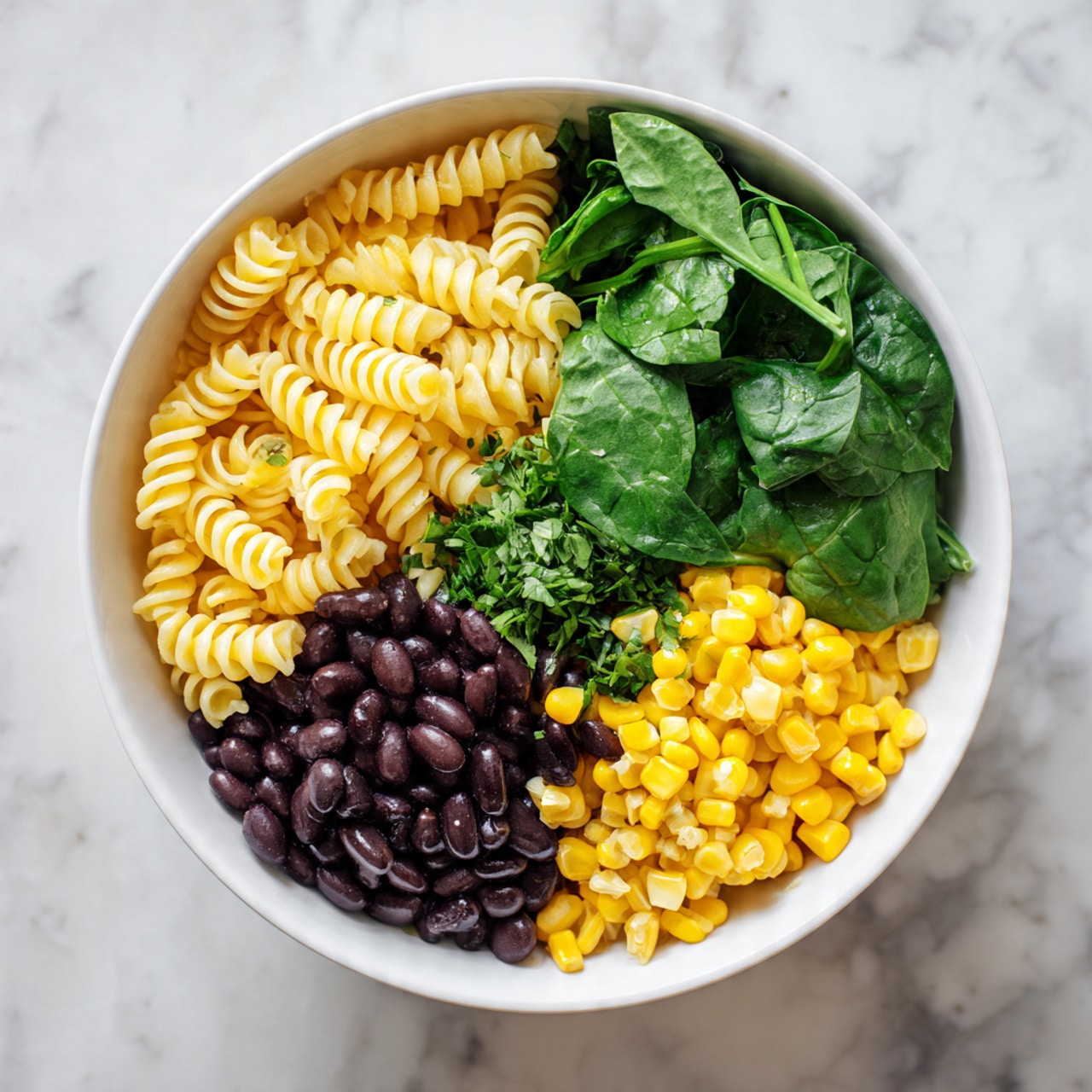 A white bowl is filled with four main layers arranged side by side. On the top left, there are tightly coiled yellow rotini pasta pieces. To the right of the pasta, there is a pile of chopped fresh spinach leaves that are deep green with a slight shine. Below the spinach, bright yellow corn kernels fill the space, looking soft and plump. On the bottom left, black beans cover the area, appearing smooth and shiny. Between the pasta and the spinach, there is a small amount of finely chopped fresh herbs with a darker green color. The bowl rests on a white marbled surface. photo taken with an iphone --ar 4:5 --v 7