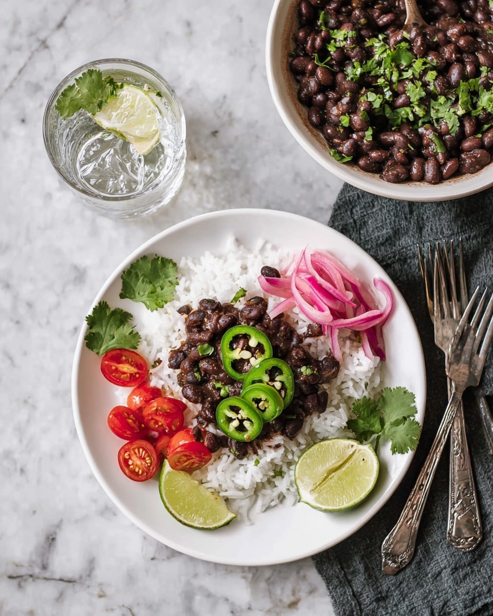 A white bowl full of dark cooked black beans mixed with bits of red sauce and sprinkled with green cilantro leaves. On top, three slices of light green jalapeño and two bright lime wedges rest. A silver spoon is partially inside the bowl on the right side. The bowl sits on a light blue plate against a white marbled surface with lime halves and cilantro leaves around it. In the back, a clear glass of water is slightly visible. Photo taken with an iphone --ar 4:5 --v 7