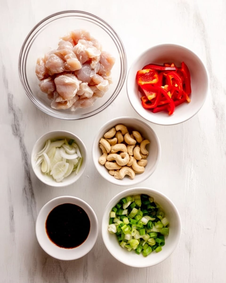 The image shows five white bowls arranged on a white marbled surface. The top left bowl is large and clear, filled with small, light pink raw chicken pieces. To the right of it is a medium white bowl holding separated slices of white onions and red bell peppers. Below them, there are three smaller white bowls; one contains whole cashew nuts with a light brown and cream color, another holds dark brown sauce, and the last one is filled with chopped green onions showing fresh green shades. photo taken with an iphone --ar 4:5 --v 7