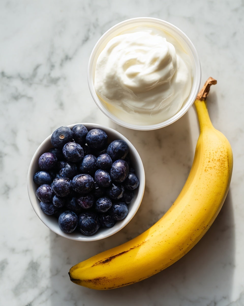 The image shows three main ingredients laid out on a white marbled surface: a white container filled with smooth, creamy Greek yogurt positioned at the top center; below it to the left is a small white bowl filled with round, plump dark blue blueberries with a slightly shiny texture; and to the right side is a whole yellow banana with some brown spots, curved gently and resting directly on the surface. The lighting is soft and natural, highlighting the colors and textures of each ingredient. Photo taken with an iphone --ar 4:5 --v 7