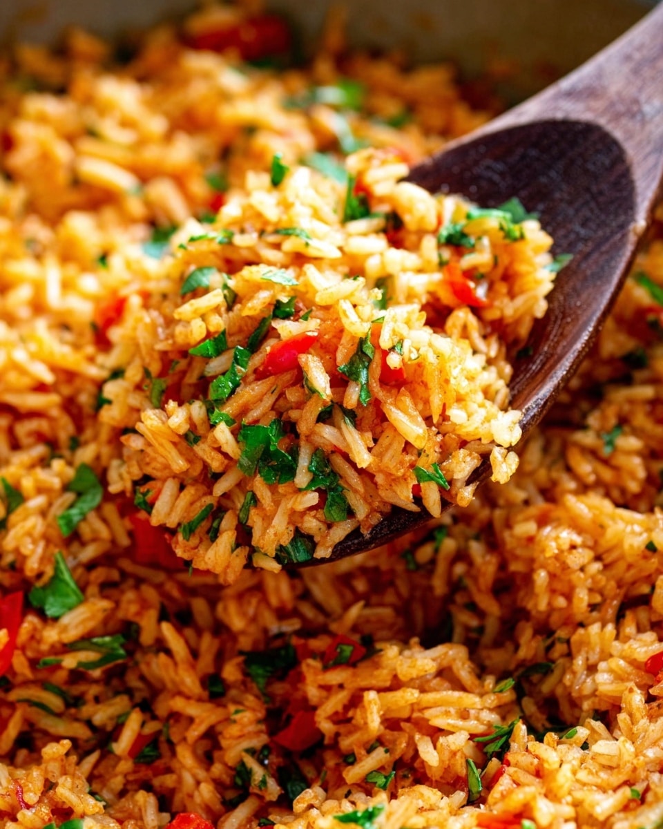 The image shows a close-up view of a wooden spoon scooping up a colorful dish of orange-brown cooked rice mixed with small pieces of red peppers and finely chopped green herbs scattered evenly throughout. The rice grains are fluffy and distinct, with a slight glossy texture, all sitting against a blurred background of more rice on a white marbled surface. The mix looks fresh and vibrant, suggesting a savory, spiced flavor. Photo taken with an iphone --ar 4:5 --v 7