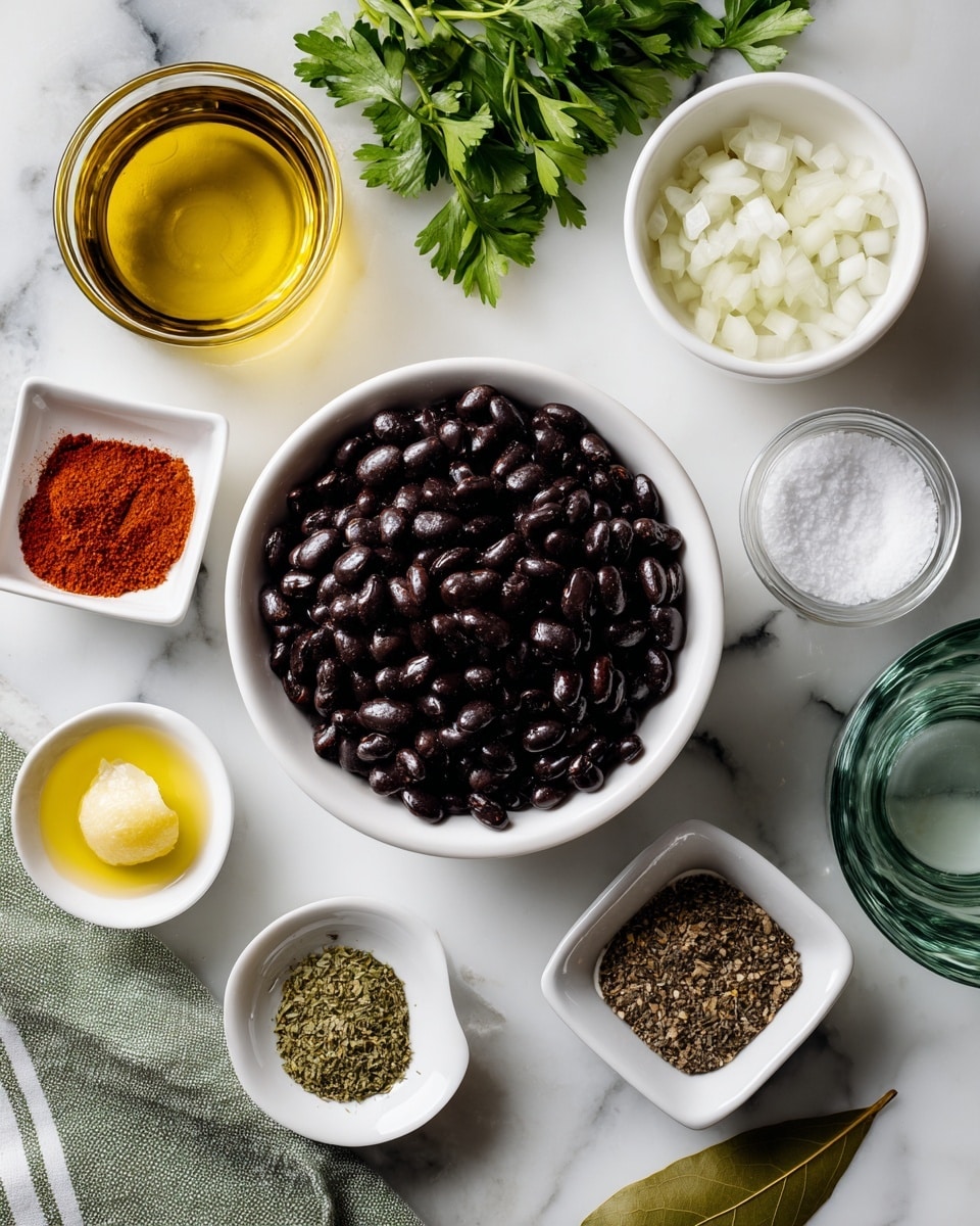 A white bowl filled with dark, shiny black beans is placed near the center on a white marbled surface. Around the bowl are small white square dishes holding different spices: bright red chili powder, green oregano, and brown cumin. A white bowl with chopped white onion sits near the top right, and a deep green bay leaf lies next to the cumin. Near the left side, a small clear glass holds light golden oil, and a white square dish contains pale minced garlic. Two small white round bowls hold yellowish lemon and lime juice, placed near the bottom left. Close to them are two clear round bowls with salt and pepper mix and plain salt. At the right middle side, a clear glass of water sits near a green striped cloth and a bit of green glass item. Some fresh green parsley is visible near the top left corner. Photo taken with an iphone --ar 4:5 --v 7