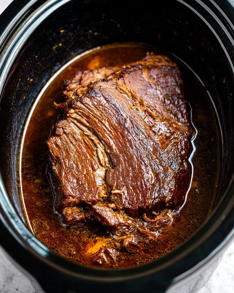 A close-up view of a single large piece of dark brown cooked meat with a slightly rough and textured surface, resting in a black oval slow cooker filled halfway with rich, glossy dark brown sauce. The meat shows visible fibers and some caramelized edges, sitting in the sauce that reflects light softly. The slow cooker is on a white marbled surface, highlighting the deep colors of the meat and sauce. Photo taken with an iphone --ar 4:5 --v 7