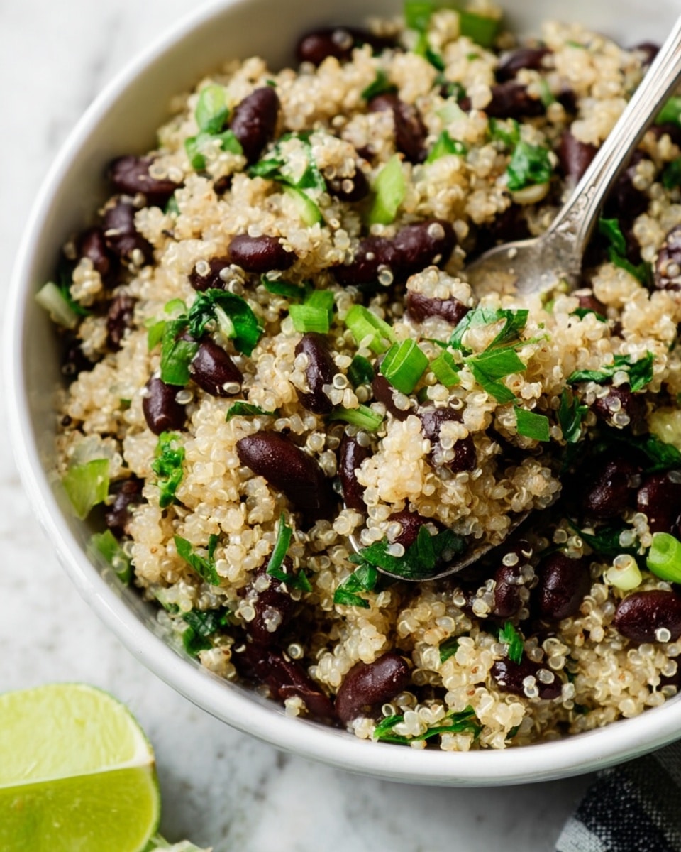 The image shows a white bowl filled with a mix of cooked light beige quinoa, dark brown beans, and scattered green herbs and sliced green onions. The quinoa looks fluffy with small round grains, while the beans add a smooth, dark texture. Green herbs and green onions are unevenly mixed throughout, adding pops of fresh green color. There is a silver spoon inside the bowl, partly scooping up the quinoa and beans mixture. In the bottom left corner, a cut lime with bright green skin and juicy light green inside sits partially visible. The bowl is placed on a white marbled surface. Photo taken with an iphone --ar 4:5 --v 7