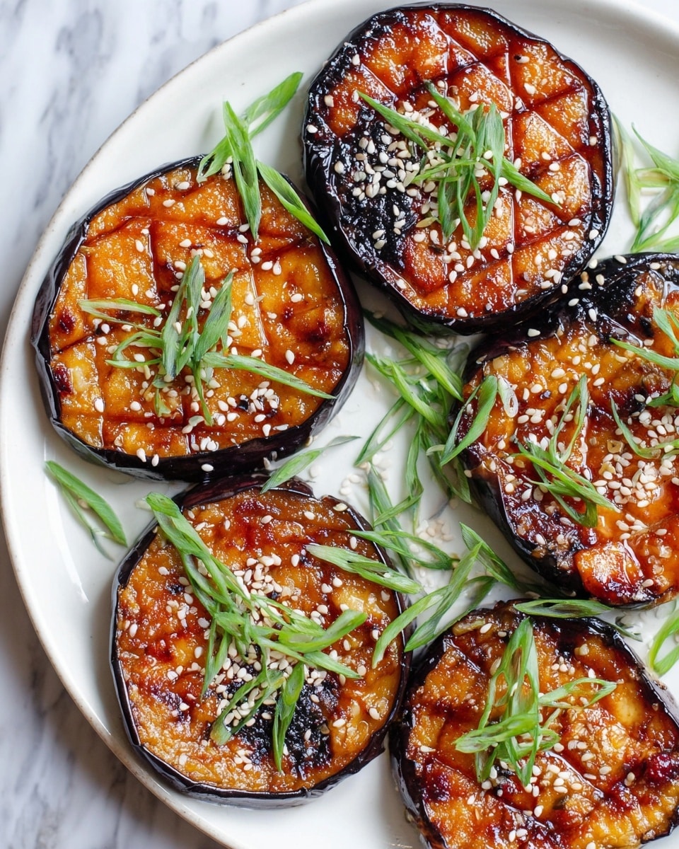 Five thick round pieces of grilled eggplant with dark purple skin and caramelized, slightly charred bright orange tops are arranged on a white plate. The tops have a glossy texture with a repeated diamond pattern scored into them, sprinkled with white and black sesame seeds. Thin green onion curls are scattered around the eggplants on the plate, adding fresh touches of bright green. The plate rests on a white marbled surface. photo taken with an iphone --ar 4:5 --v 7