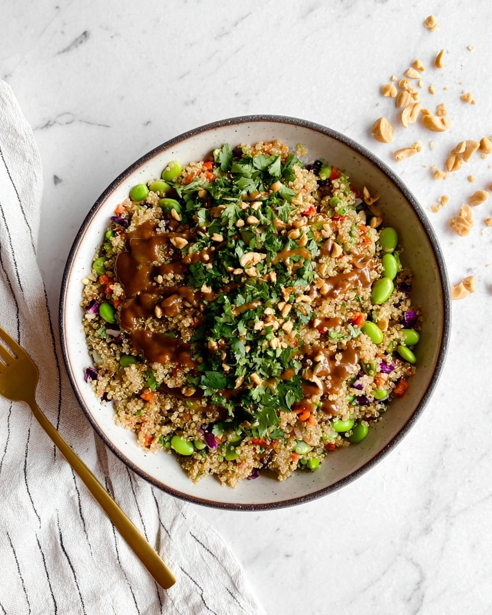A white bowl filled with a colorful quinoa salad sitting on a white marbled surface. The salad has a base layer of light beige quinoa mixed with bright green edamame beans and pieces of red bell pepper, all mixed evenly throughout. On top, there are thin slices of purple red onion, small green cilantro leaves scattered all over, and chopped peanuts adding a crunchy texture. Two lime wedges rest on one side of the bowl, adding a fresh touch. A silver spoon is placed inside the bowl, angled towards the salad. Photo taken with an iphone --ar 4:5 --v 7