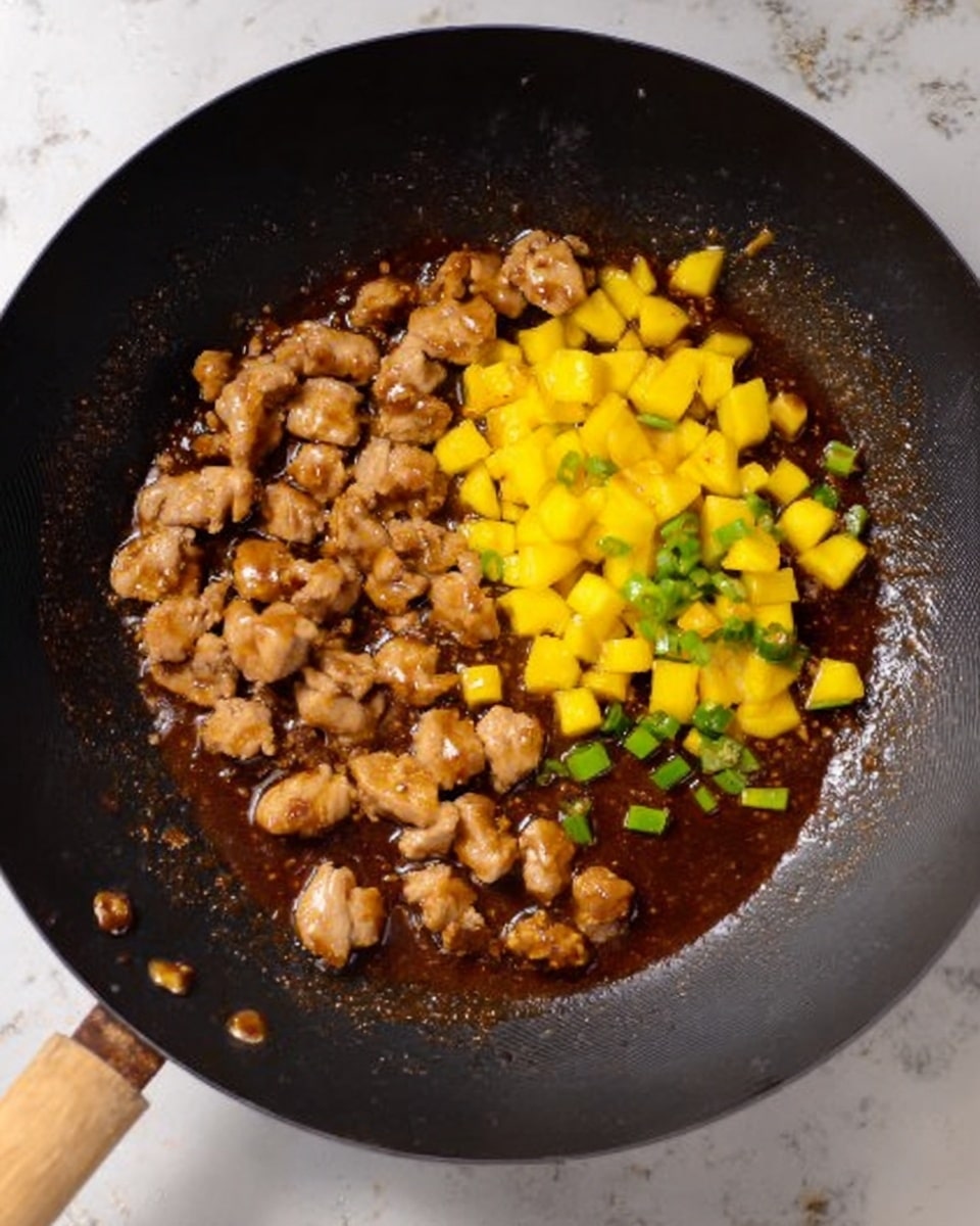 The image shows a black wok with a wooden handle placed on a white marbled surface. Inside the wok, there is a rich brown sauce covering the bottom. On one side, small pieces of cooked light brown meat are spread out, while on the other side there are bright yellow diced pieces of fruit or vegetable. There are some small green slices mixed in the sauce, adding color contrast. The texture of the sauce looks slightly thick and shiny. photo taken with an iphone --ar 4:5 --v 7