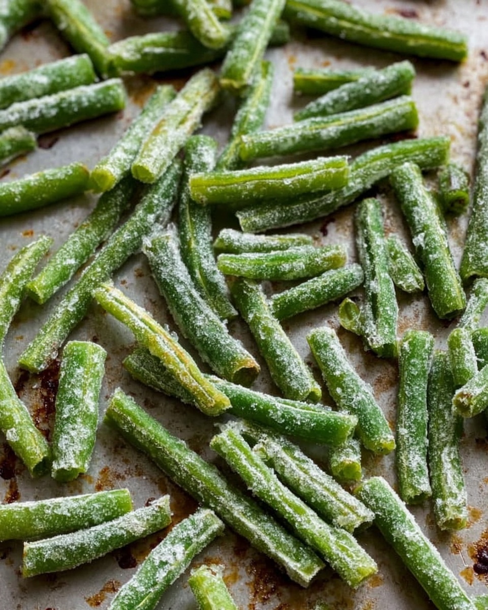 Close-up view of many small frozen green bean pieces spread out unevenly on a layer of white parchment paper, which is placed on a white marbled countertop. The beans are short, cut into small chunks, showing a rough texture with some frost. The background is softly blurred with natural light, giving a fresh and cool look to the image. Photo taken with an iphone --ar 4:5 --v 7