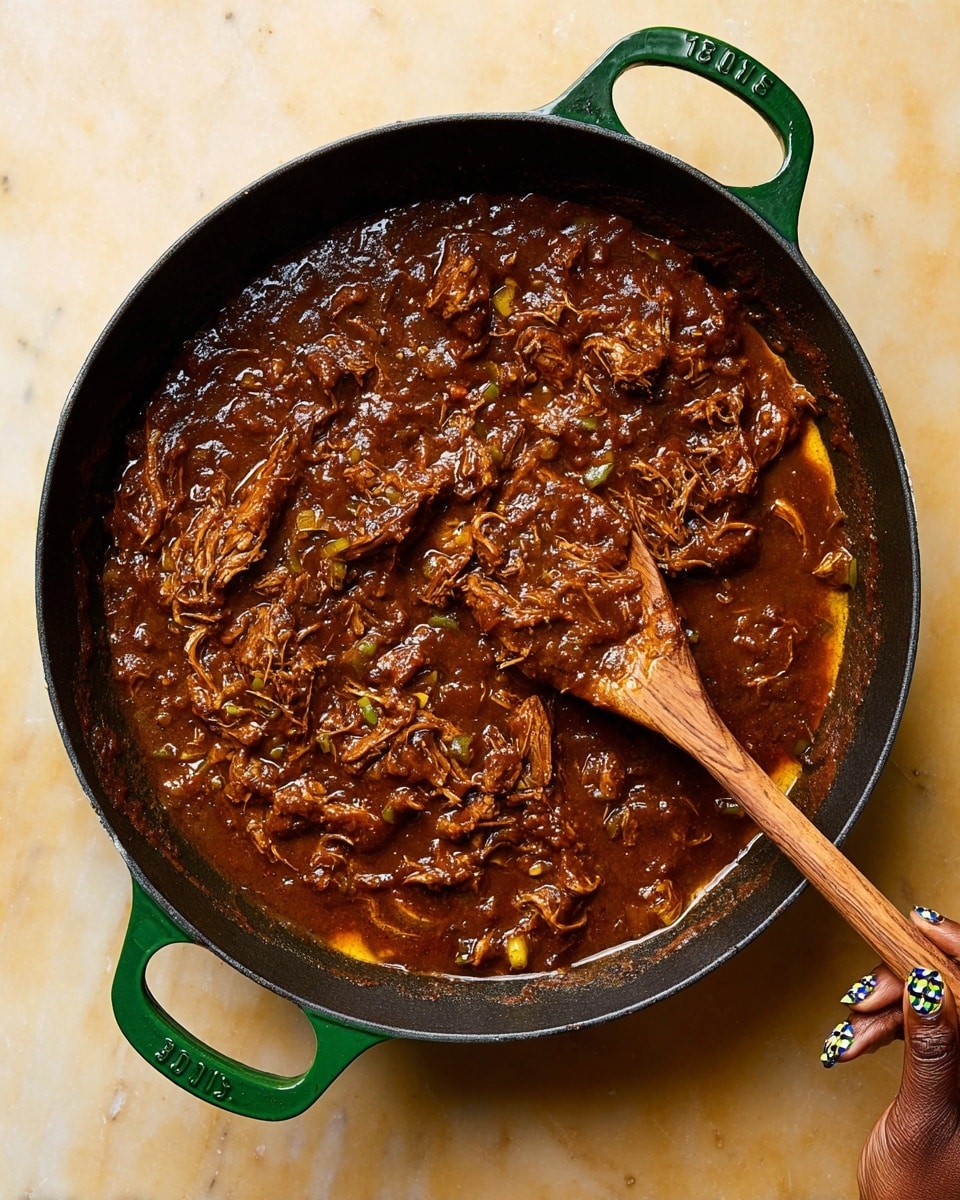A green cast iron skillet filled with thick dark brown stew that holds shredded pieces of meat and small bits of onions and peppers, with a wooden spoon stirring the rich sauce on the right side; a woman's hand is holding the skillet’s handle at the bottom of the image, showing dark skin and decorative printed nails. The surface under the skillet is a white marbled texture. photo taken with an iphone --ar 4:5 --v 7