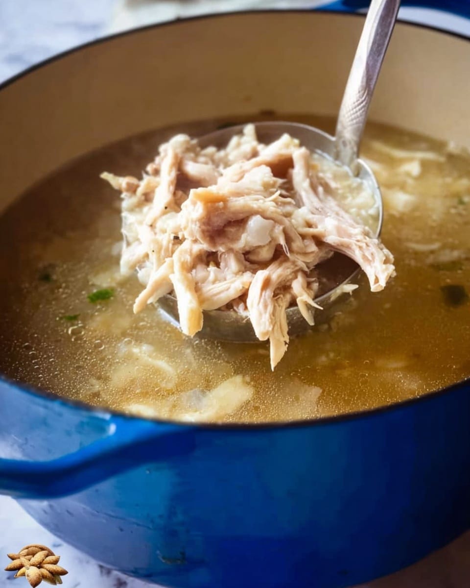 A close-up view of a large blue pot filled with clear broth soup. A silver ladle lifts a mix of light beige shredded chicken and short white noodles from the pot. The chicken pieces have a soft, fibrous texture, and the broth appears thin and hot, slightly steaming. The background and surface are a white marbled texture. photo taken with an iphone --ar 4:5 --v 7